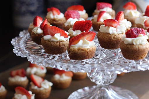 A glass tray filled with little sponge cake smothered in cream and topped with a strawberry.